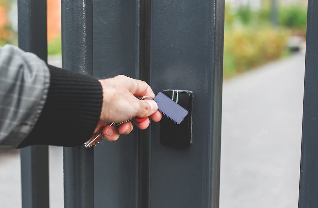 Hand with an electronic key fob near an access control reader on a metal gate